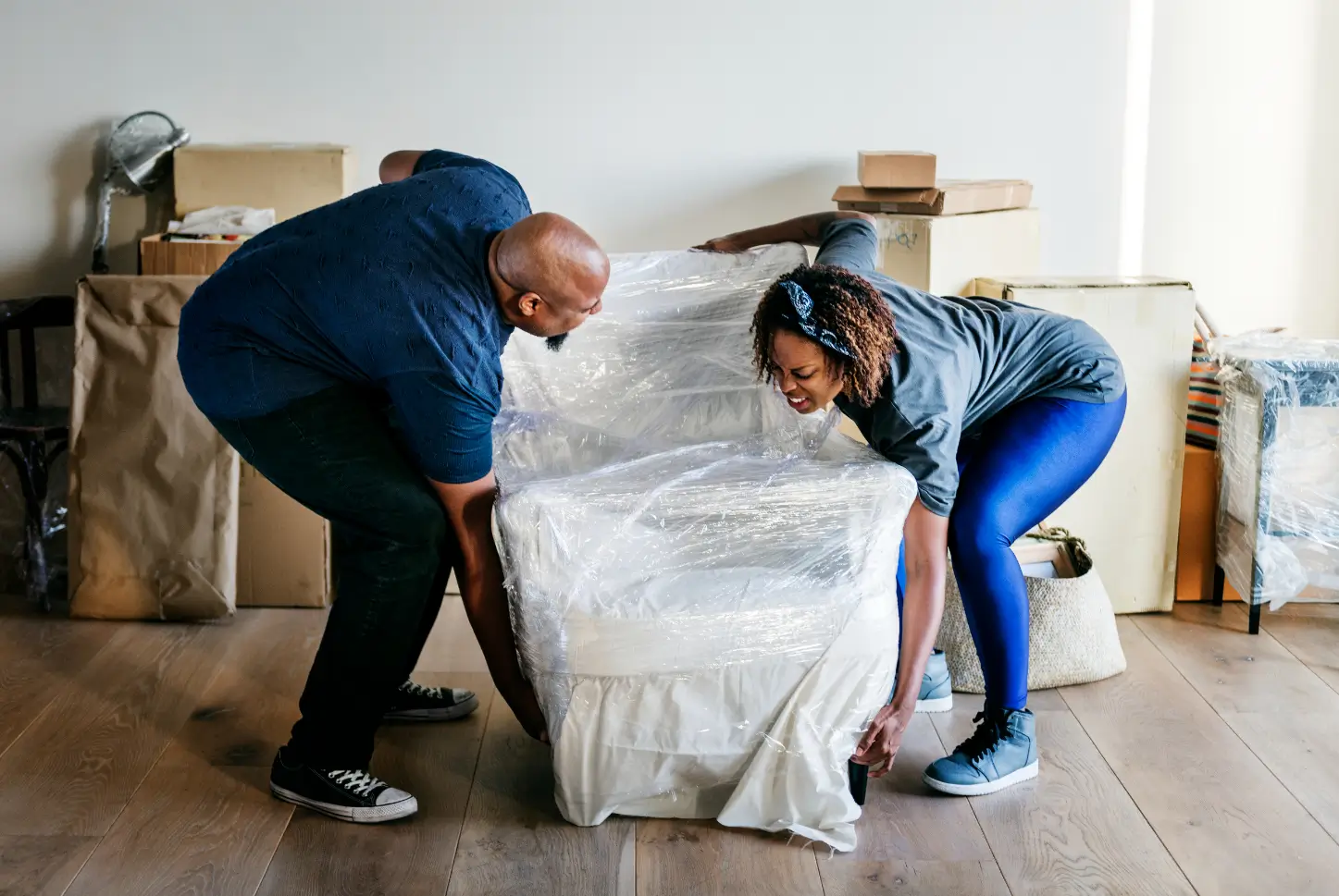 Two people lifting and wrapping furniture during packing and moving assistance services in Dover, Delaware.